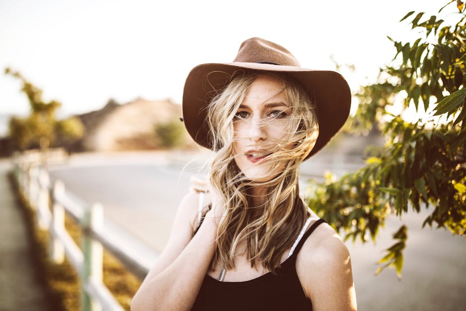 A young woman in a hat poses outdoors on a sunny day, blending fashion and natural beauty.
