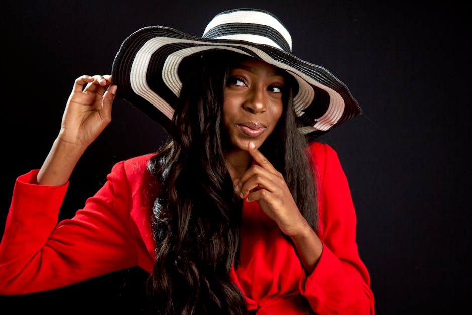 Elegant portrait of a woman in a red outfit and striped wide brim hat, exuding fashion and style.