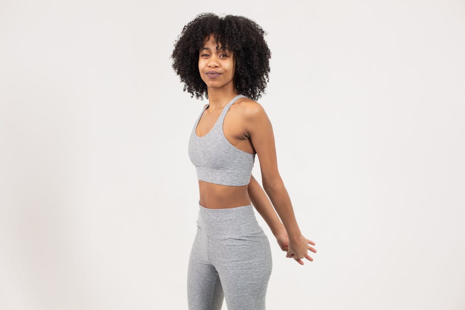 Young woman with curly hair stretching in sportswear on a white background.
