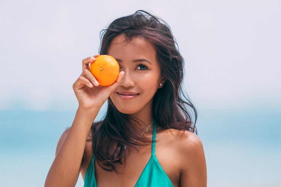 Young woman in swimwear holding an orange, enjoying a sunny day by the sea.