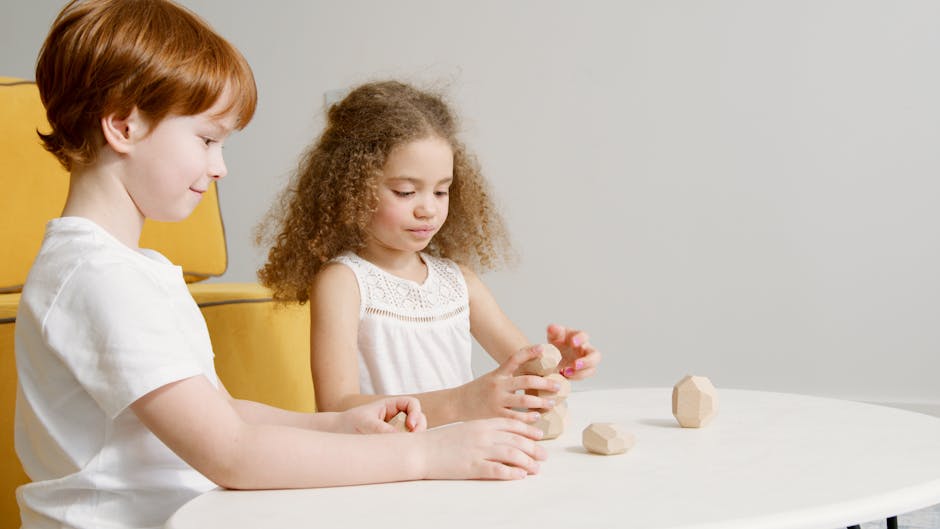 Two kids enjoying stacking wooden geometric blocks at a table indoors.