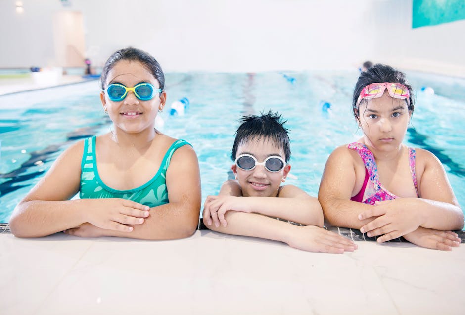 Three smiling children in swimwear enjoying a swim at an indoor pool. Perfect for lifestyle and leisure themes.