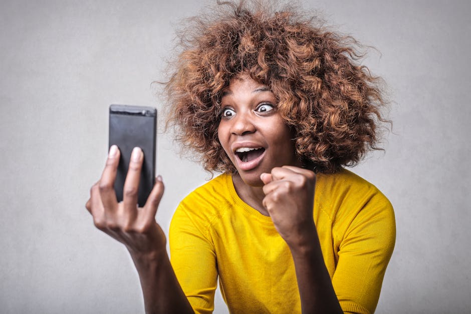 Joyful woman in yellow showing surprise and excitement at smartphone message indoors.