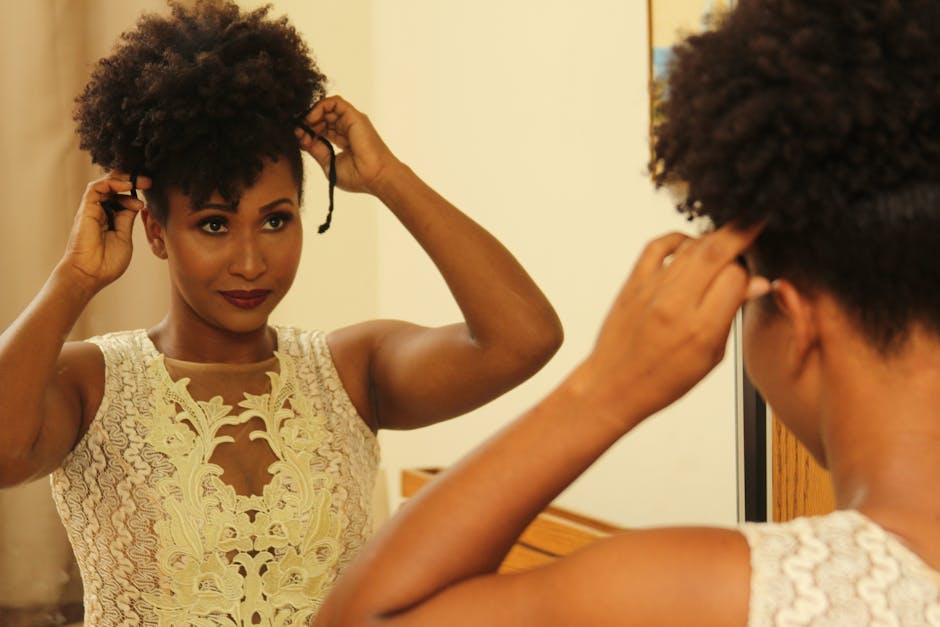 Chic black woman in lace dress adjusting her hairstyle in front of a mirror, exuding grace and beauty.