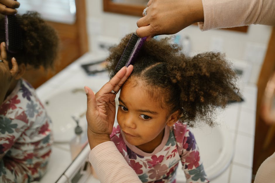 A mother styles her young daughter's hair in front of a bathroom mirror with gentle care