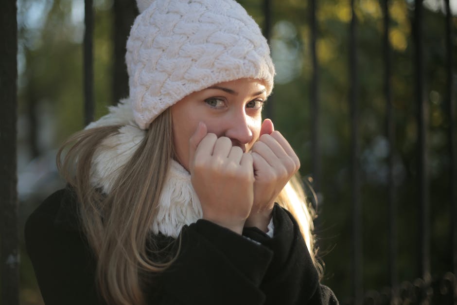 Close-up portrait of a woman smiling warmly, wearing a knit hat and coat, enjoying a winter day outdoors.