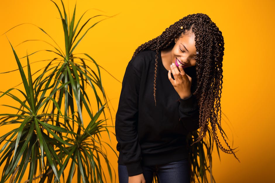 Cheerful young African American woman with Afro hairstyle touching lips while laughing against yellow background and looking down
