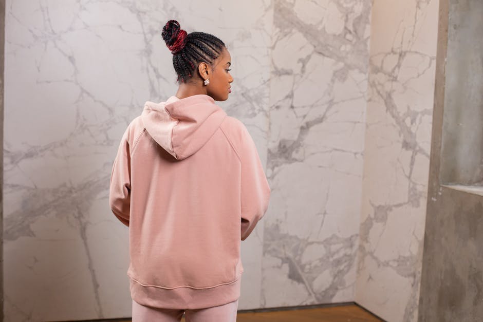 Rear view of a young woman in a pink hoodie standing indoors, showcasing her braided hairstyle.