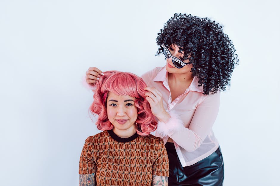 Two women having fun with colorful wigs and playful styling in a studio setting.