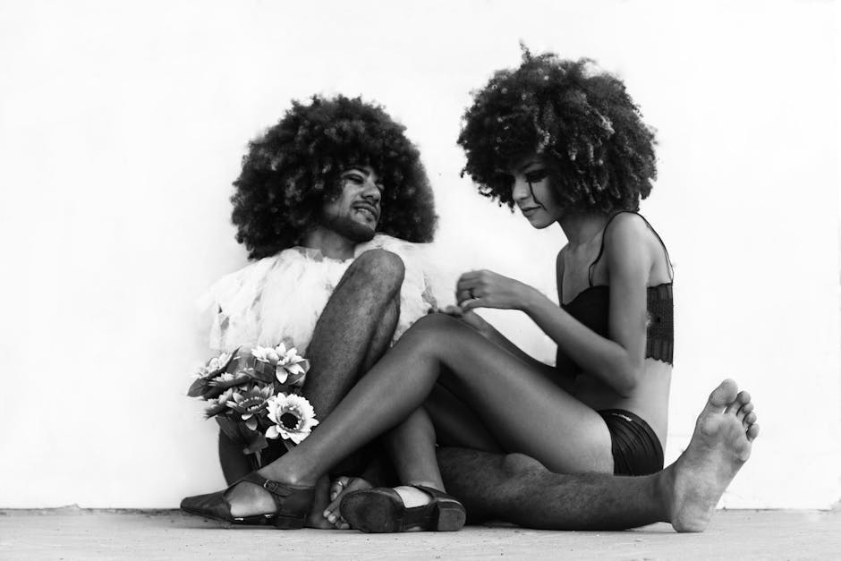 Creative, black and white portrait of two individuals with afro hairstyles sitting on the floor.