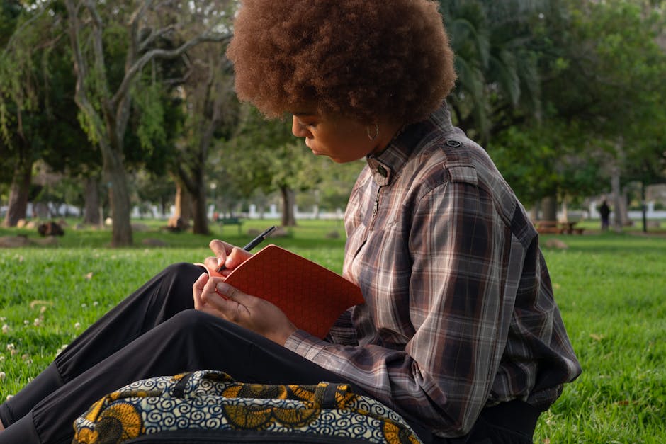 A young woman with curly hair writing in a notebook outdoors, embodying leisure and creativity.