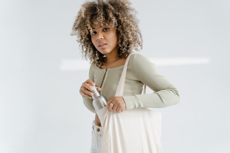 Stylish African American woman placing a bottle in her beige tote bag during a studio shoot.