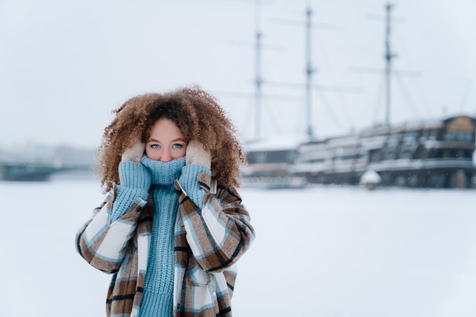 Portrait of a woman in a blue sweater and plaid coat in a snowy outdoor setting.
