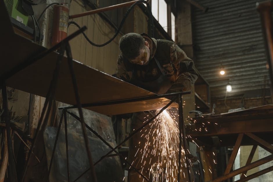 A worker focused on welding metal inside an industrial setting with sparks flying.