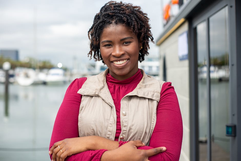 Portrait of a smiling woman with dreadlocks standing confidently at a marina, exuding warmth and confidence.