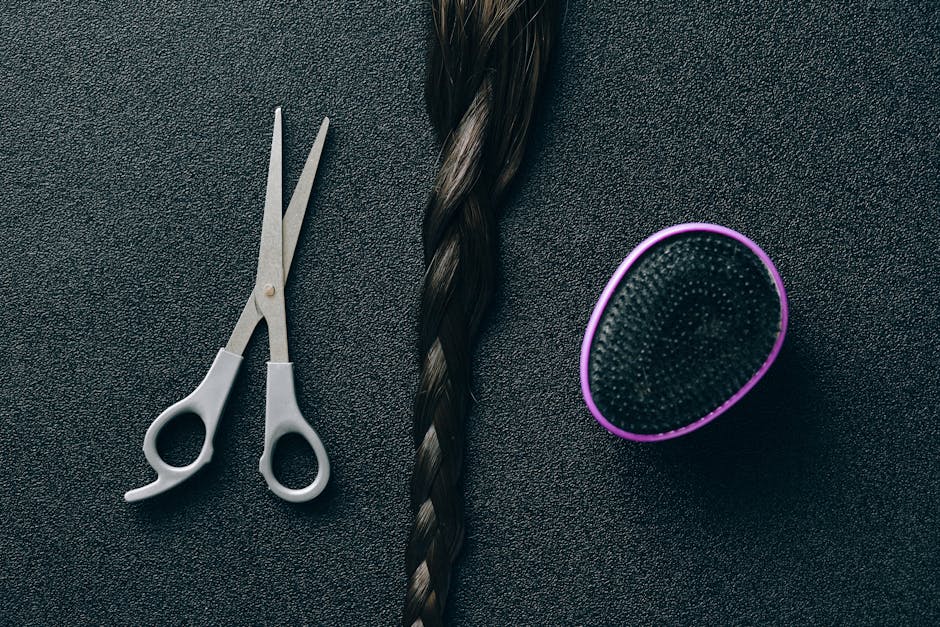 Close-up of hairdressing scissors, braided hair, and brush on black background.