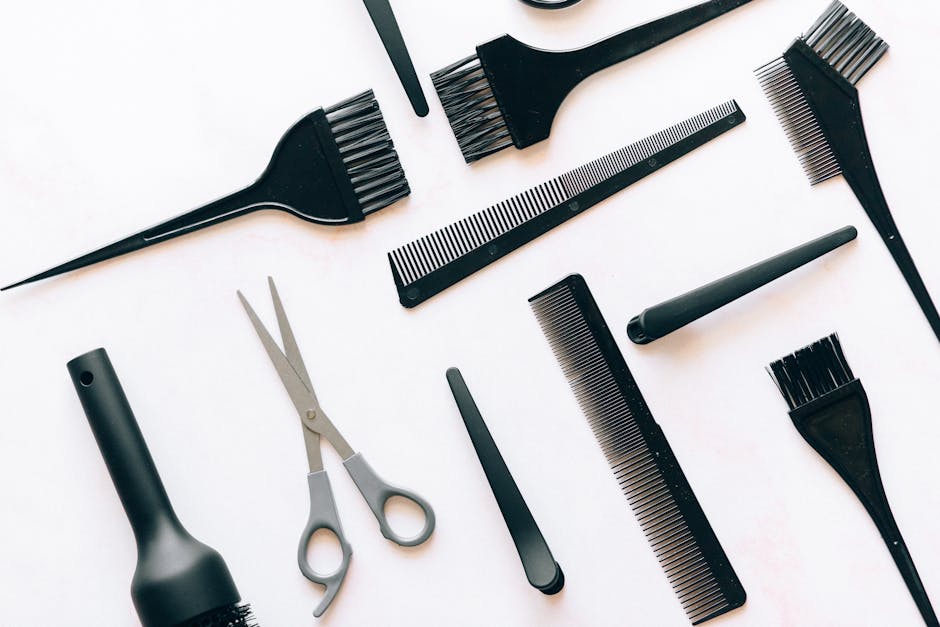 Flat lay of essential hairdressing tools including brushes, combs, and scissors on white background.
