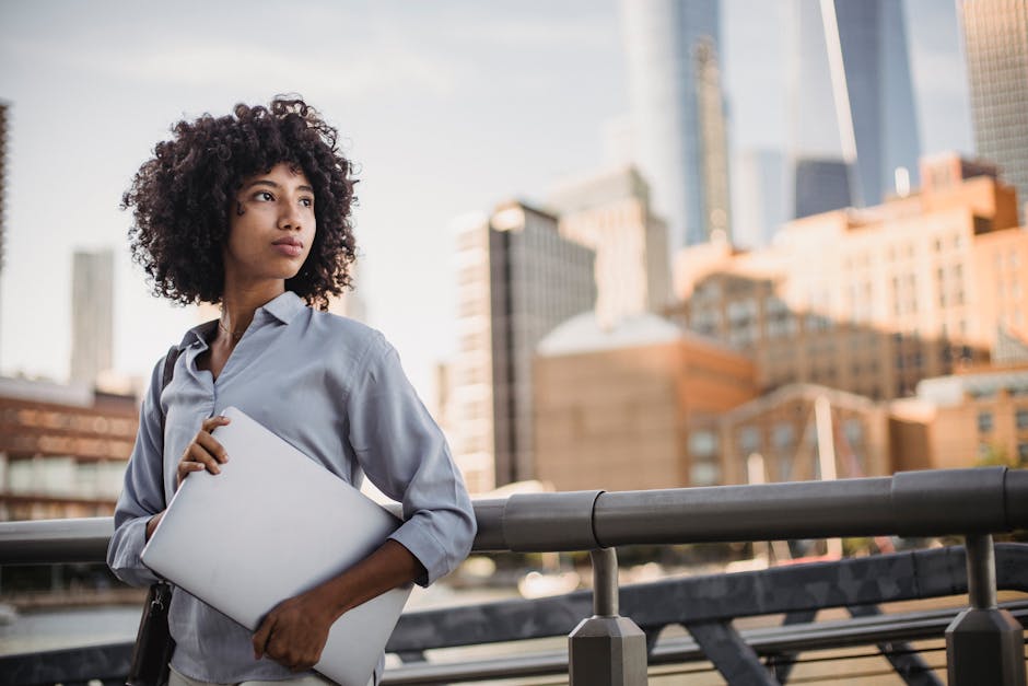Confident woman in business attire holding a laptop in an urban outdoor setting.