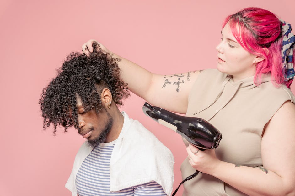 A hairstylist blow-dries a man's curly afro hair in a studio setting.