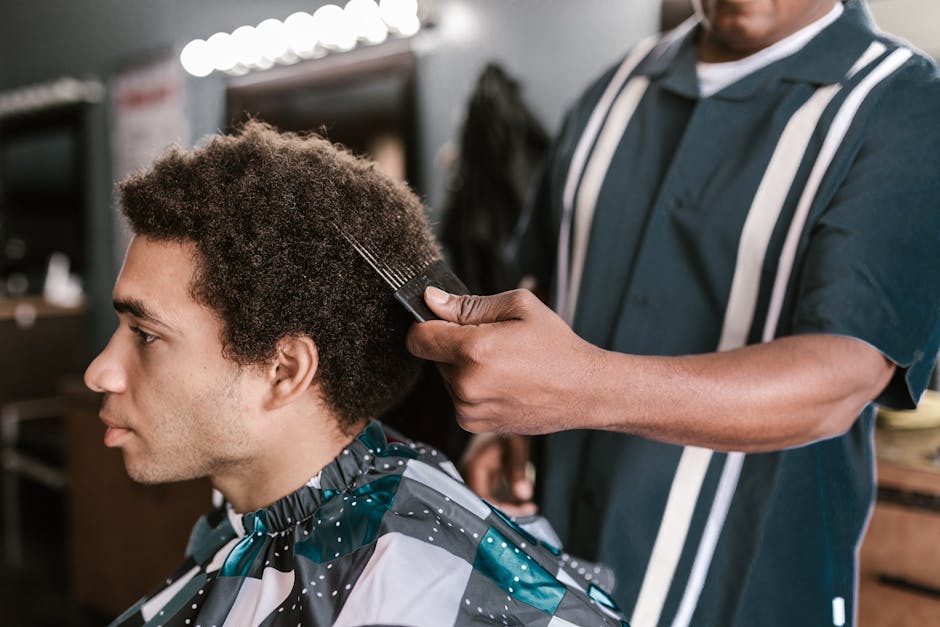 A barber uses an afro pick to style a client's hair in a modern barbershop setting.