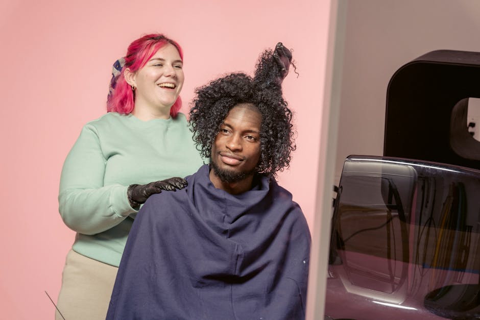 Positive African American female hairdresser hairstyling African American male customer in studio with light pink wall