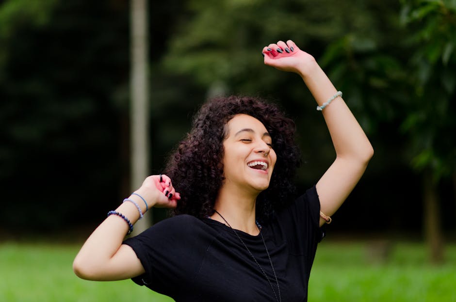 A woman joyfully raising her arms in a green park, expressing happiness and freedom.
