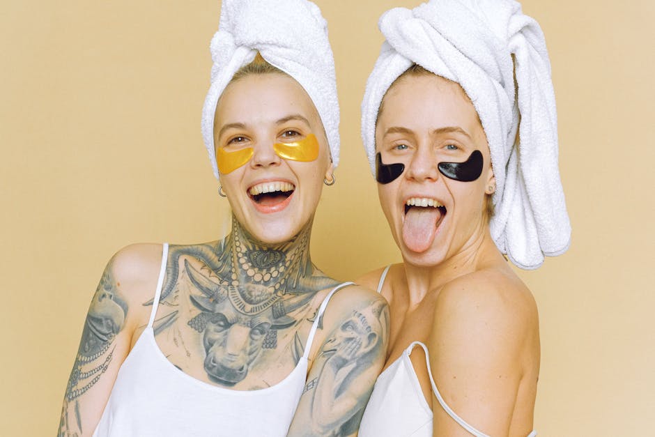 Two women enjoying a lively skincare routine with eye masks and towels on heads.