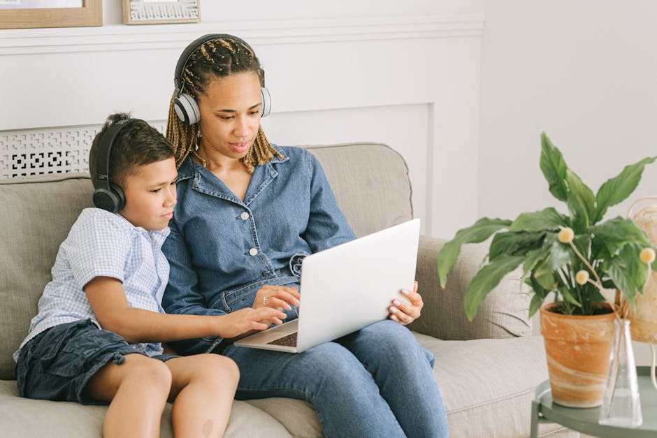 A mother and son with headphones using a laptop on a couch, enjoying quality time indoors.