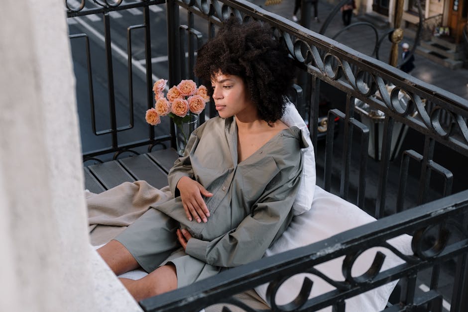 Serene portrait of a pregnant woman sitting on a cozy balcony in the city with flowers nearby.