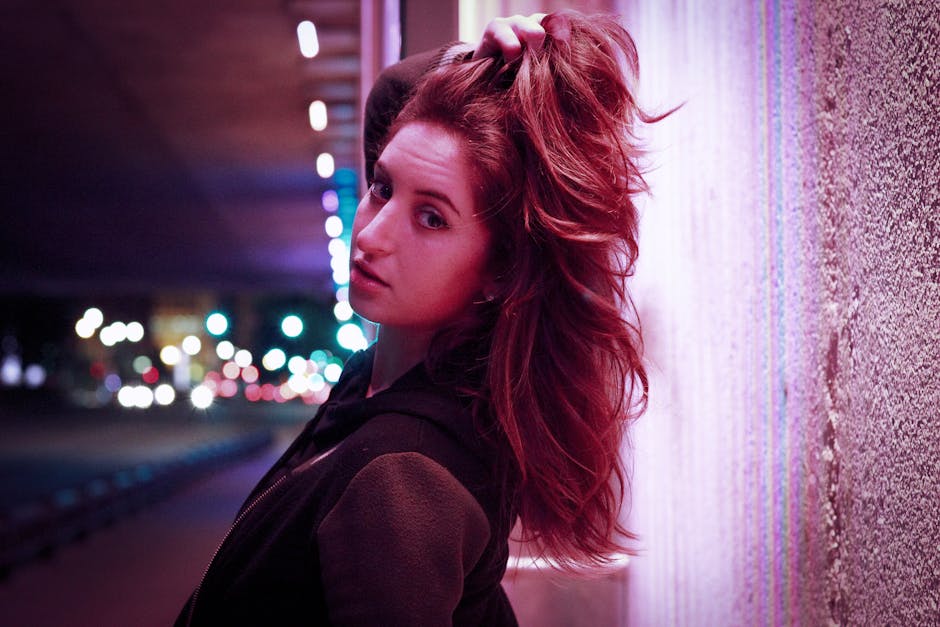 Stylish young woman poses in a moody urban setting with vibrant lighting.