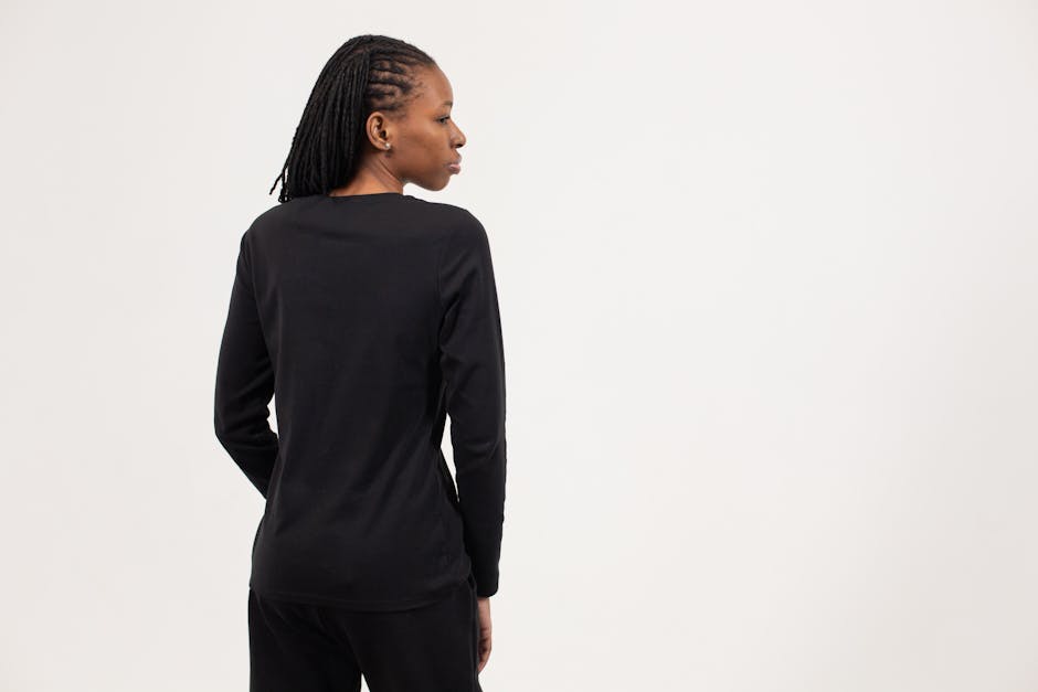 Back view of self assured young ethnic lady with Afro braids in total black outfit standing against white background and looking away