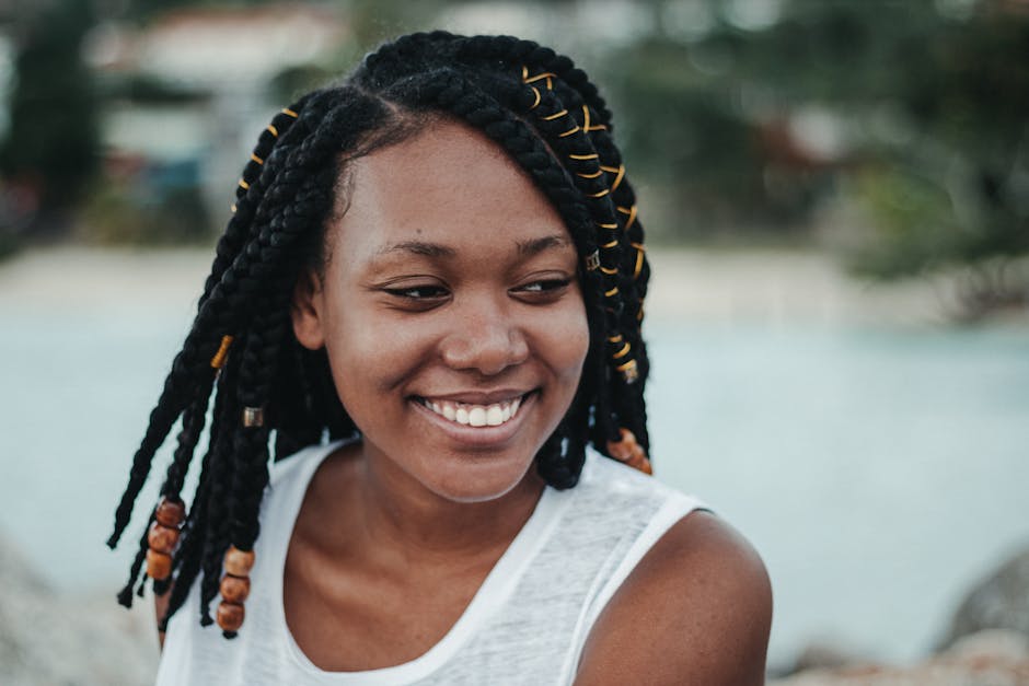 Young happy ethnic female with Afro braids looking away near river in summer