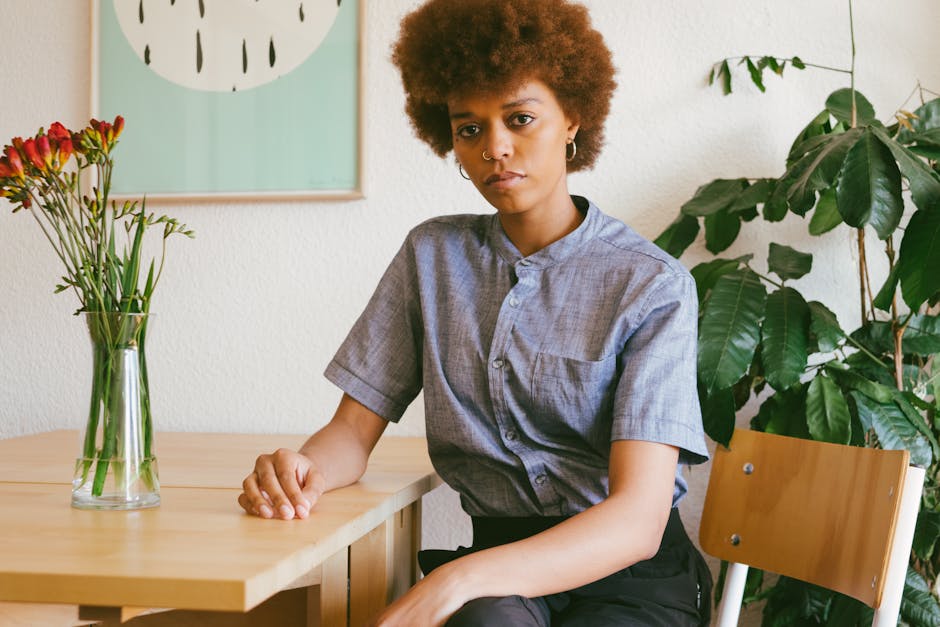 Stylish woman with afro hairstyle sitting indoors, showcasing fashion with piercing and modern decor.