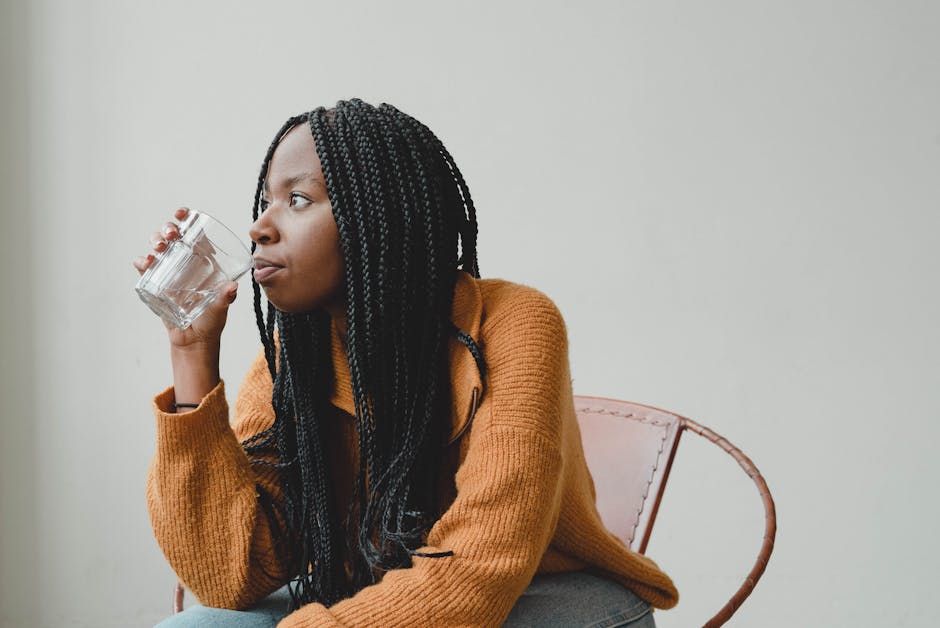 A serene young woman in a cozy sweater, sipping water and pondering indoors.